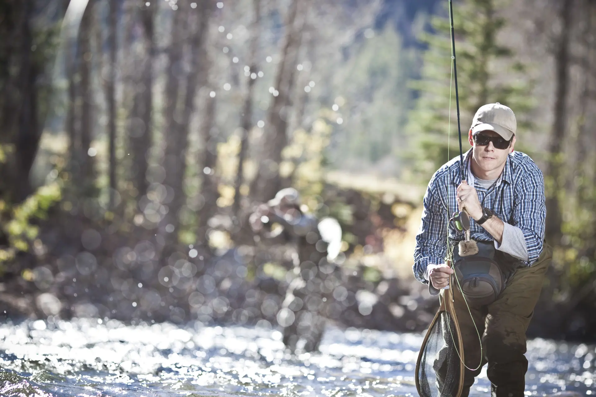 Fly angler fishing in a sunlit wooded river