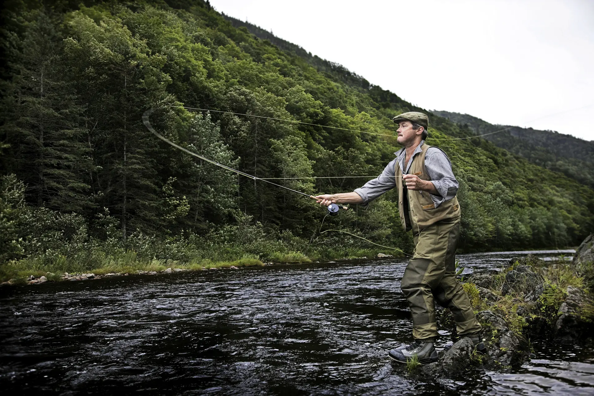 Fly angler casting on a wooded Scottish river